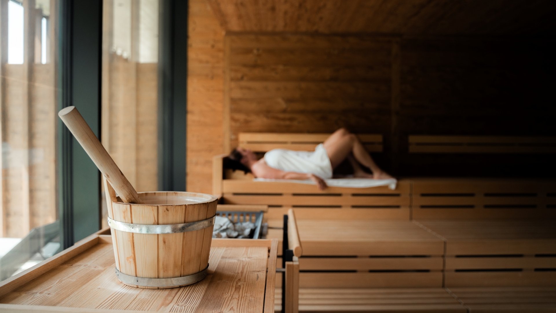 Sauna with woman relaxing on wooden benches wrapped in towel